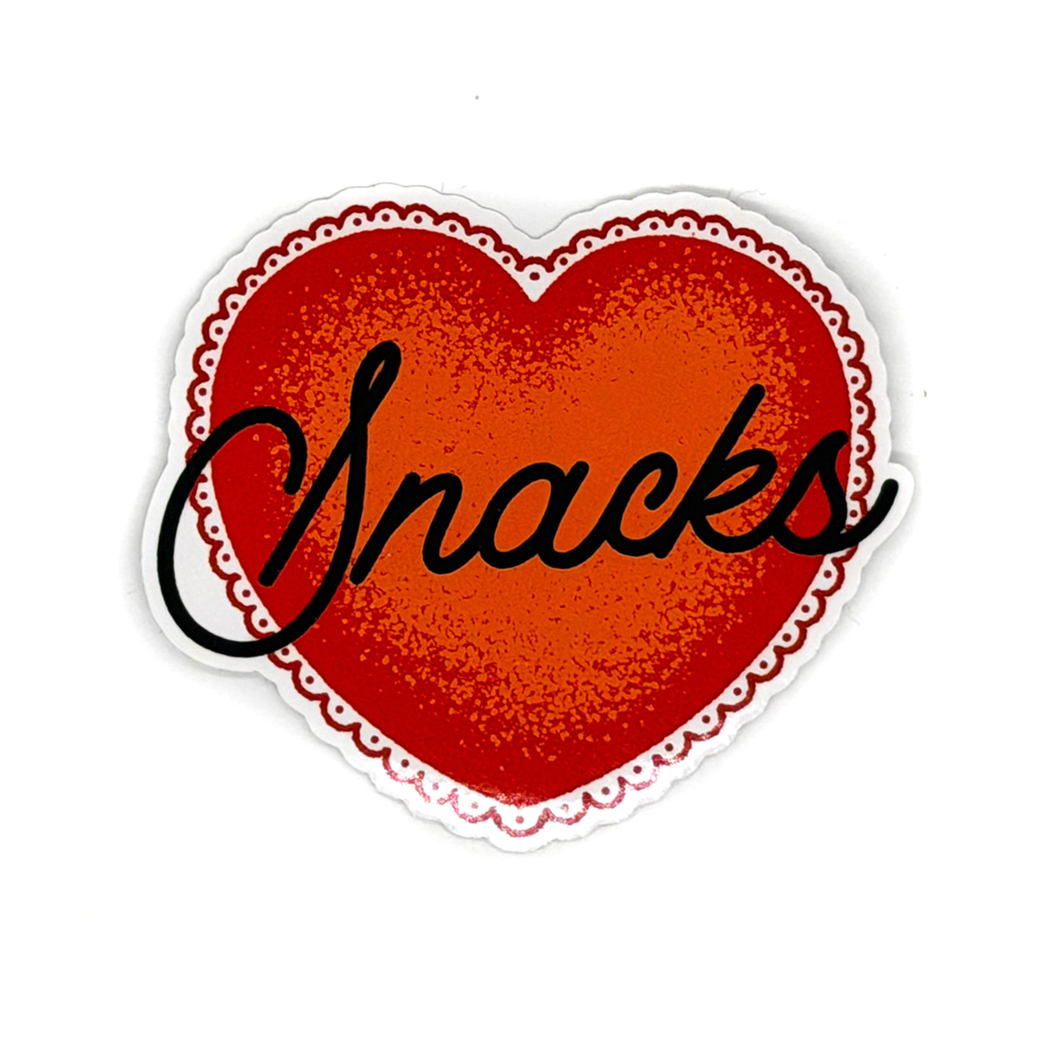 A heart-shaped sticker or decal with a red textured center, a scalloped white border, and the word 'Snacks' written across it in black script, shown on a plain white background.