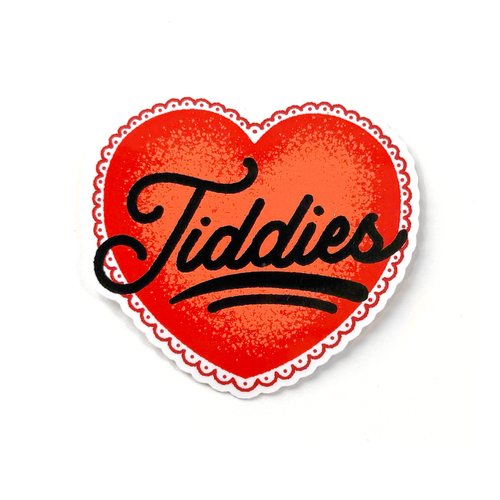 Red heart sticker with black hand-drawn script typography reading “Tiddies” in a clean, minimalist style.